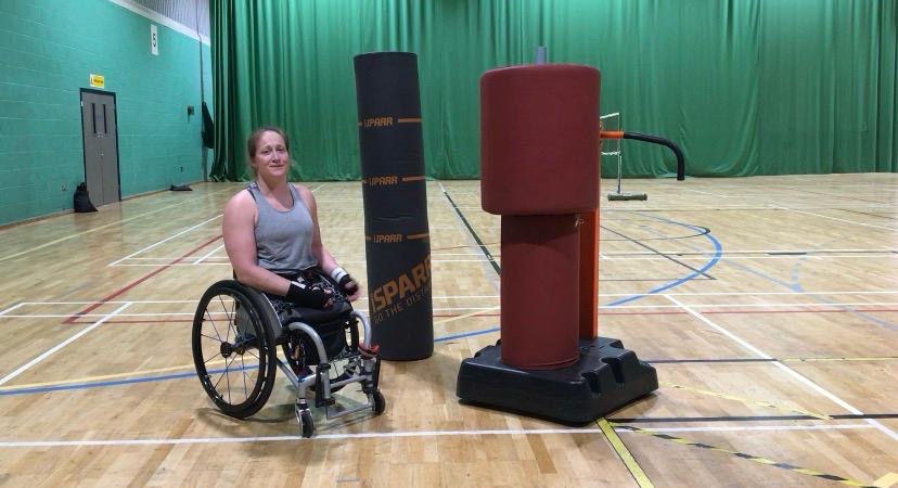 A wheelchair user training with the iSPARR adaptive bag in a sports hall